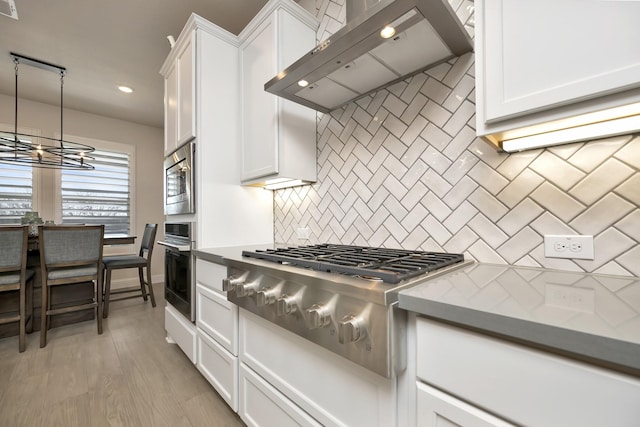 kitchen with backsplash, appliances with stainless steel finishes, light wood-style floors, white cabinets, and wall chimney exhaust hood