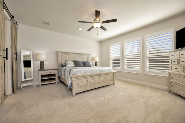 bedroom with visible vents, baseboards, light colored carpet, a barn door, and a ceiling fan