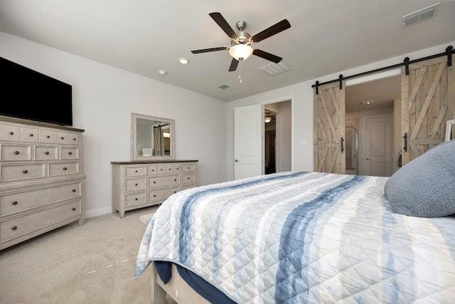 bedroom with visible vents, light colored carpet, a ceiling fan, and a barn door