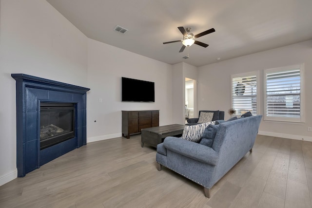 living area with visible vents, ceiling fan, baseboards, light wood-style floors, and a glass covered fireplace