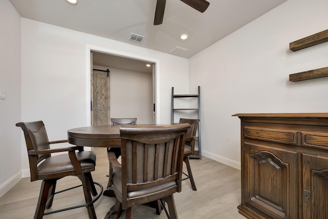 dining space with a barn door, light wood-style flooring, baseboards, and visible vents