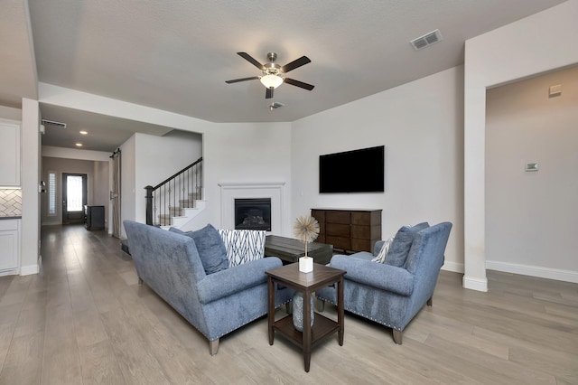 living room featuring visible vents, baseboards, light wood-type flooring, and a ceiling fan