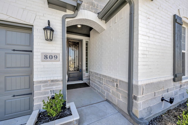 view of exterior entry featuring brick siding and a garage