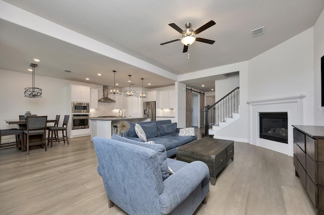 living room featuring visible vents, ceiling fan, a glass covered fireplace, and light wood-style floors
