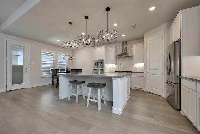 kitchen with visible vents, white cabinets, appliances with stainless steel finishes, wall chimney range hood, and tasteful backsplash