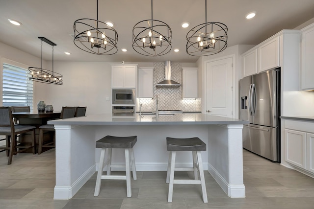 kitchen featuring white cabinets, stainless steel appliances, an island with sink, and wall chimney range hood