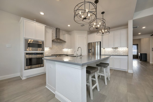 kitchen featuring visible vents, wall chimney range hood, a center island with sink, stainless steel appliances, and a sink