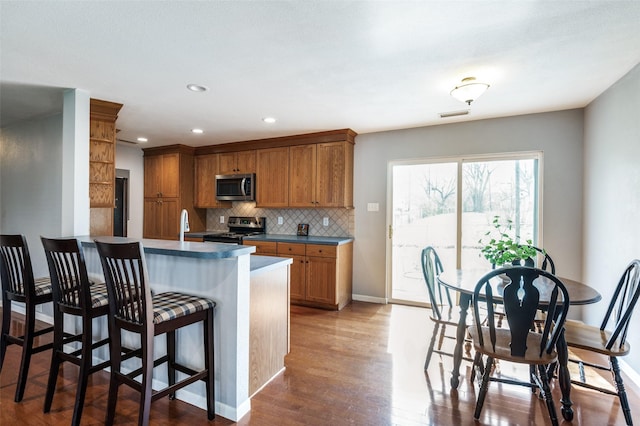 751 E Cooper St, Van Alstyne, TX 75495 - kitchen with stainless steel appliances, brown cabinets, wood finished floors, a kitchen bar, and tasteful backsplash