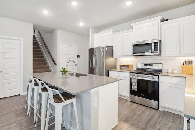 kitchen with tasteful backsplash, light wood finished floors, a center island with sink, appliances with stainless steel finishes, and a sink