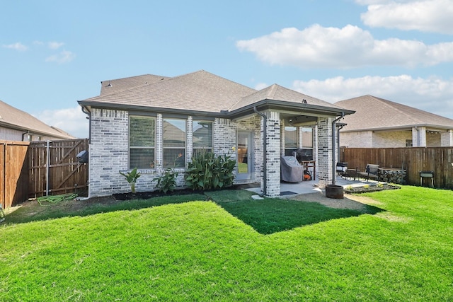 back of house featuring a lawn, a fenced backyard, brick siding, and a patio area