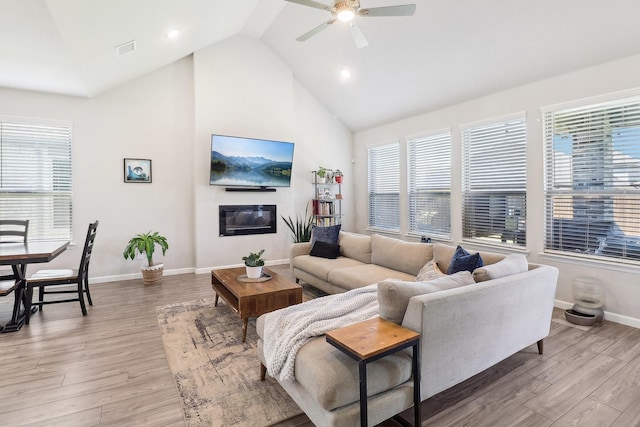 living room featuring visible vents, a ceiling fan, light wood-style floors, and a glass covered fireplace