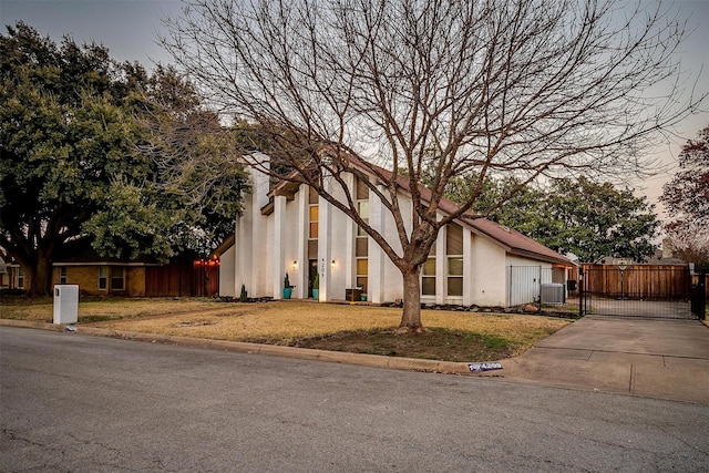 view of front of house featuring a front yard, a gate, fence, stucco siding, and central air condition unit