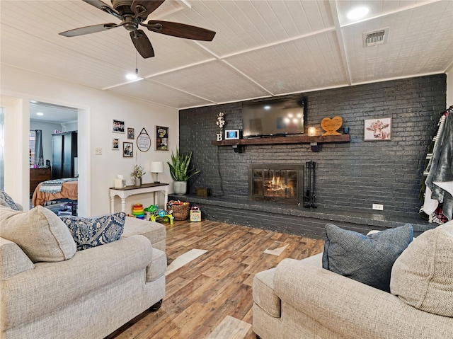 living room featuring visible vents, brick wall, ceiling fan, a fireplace, and wood finished floors