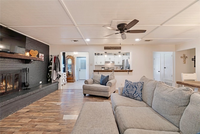 living room featuring light wood finished floors, visible vents, a fireplace, and ceiling fan