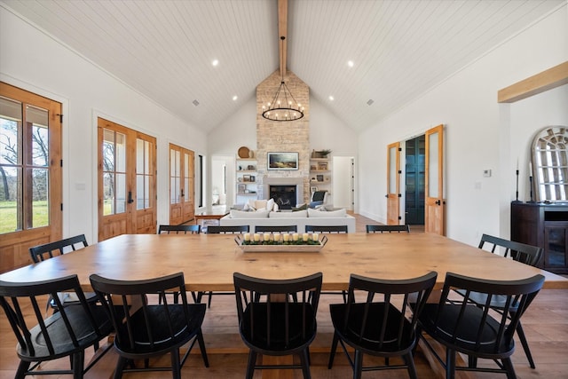 dining area with beamed ceiling, high vaulted ceiling, wood finished floors, an inviting chandelier, and a fireplace