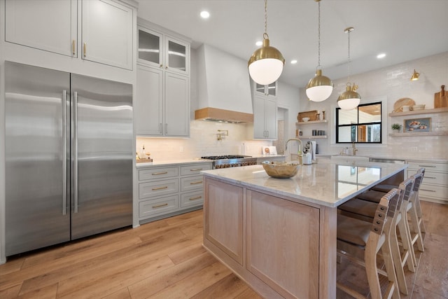 kitchen featuring tasteful backsplash, premium range hood, light wood-style flooring, stainless steel appliances, and open shelves