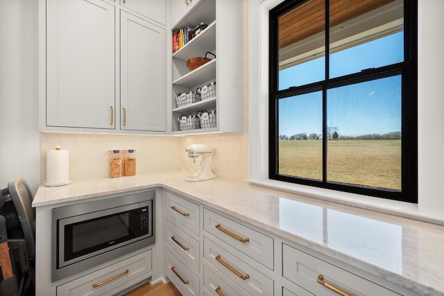 kitchen with open shelves, stainless steel microwave, light stone counters, and tasteful backsplash