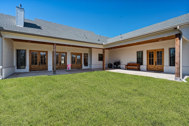 rear view of house with french doors, a yard, a patio area, and a shingled roof