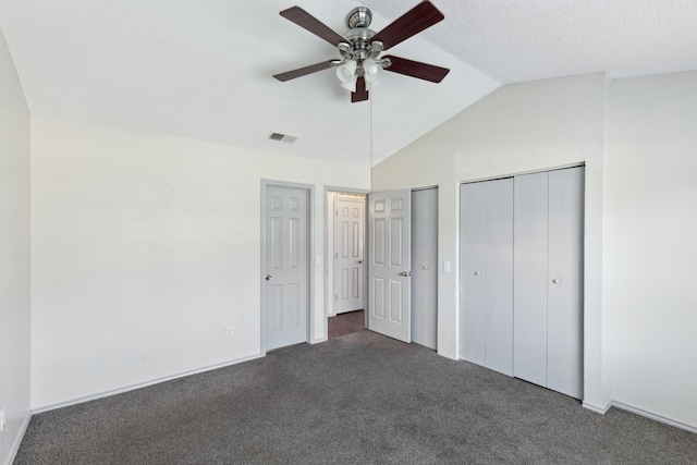 unfurnished bedroom featuring visible vents, lofted ceiling, dark carpet, ceiling fan, and two closets