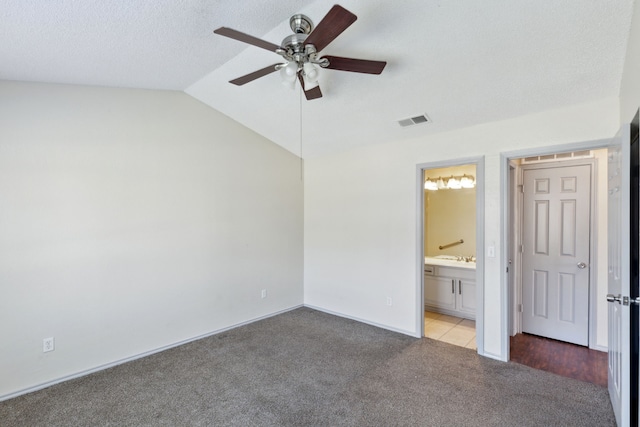 unfurnished bedroom featuring visible vents, ensuite bath, vaulted ceiling, a textured ceiling, and carpet flooring