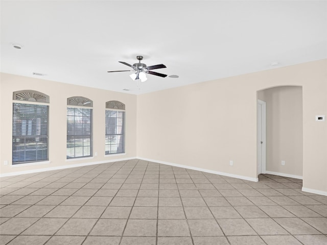 empty room featuring a ceiling fan, baseboards, visible vents, light tile patterned flooring, and arched walkways