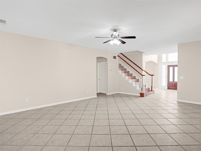 unfurnished living room featuring baseboards, light tile patterned flooring, arched walkways, ceiling fan, and stairs