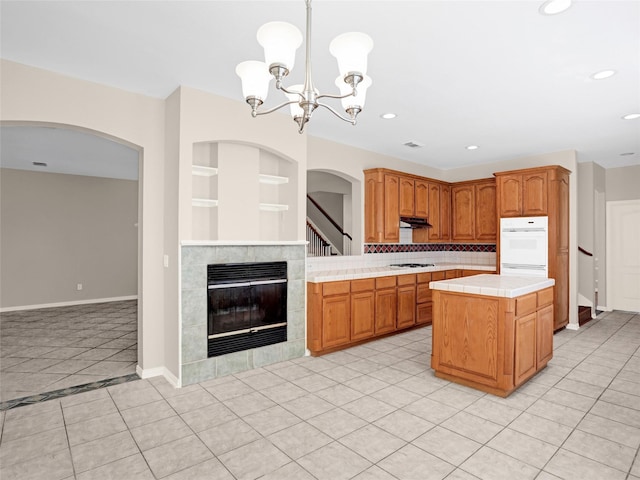 kitchen with white gas cooktop, built in features, tile counters, under cabinet range hood, and a center island