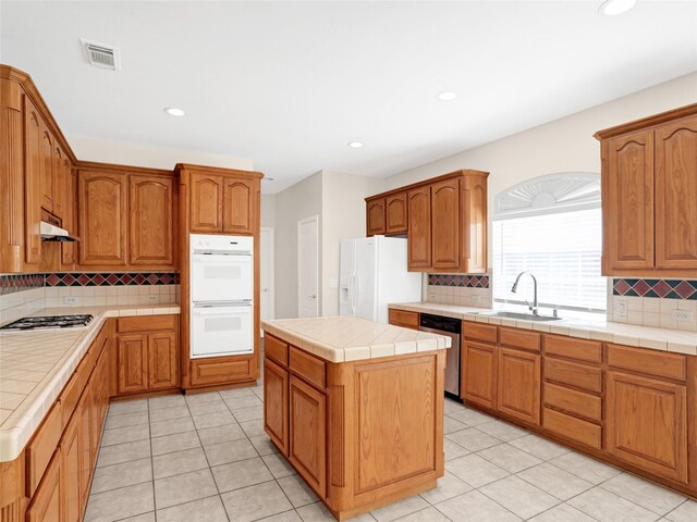 kitchen with visible vents, a sink, under cabinet range hood, tile countertops, and appliances with stainless steel finishes