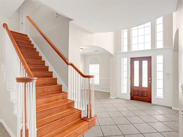 entryway with stairway, arched walkways, baseboards, and light tile patterned flooring