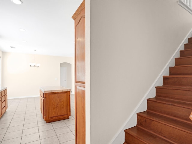 staircase with tile patterned flooring, an inviting chandelier, arched walkways, and baseboards