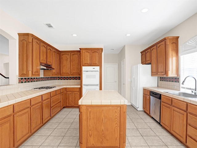 kitchen with white appliances, visible vents, a sink, under cabinet range hood, and a center island