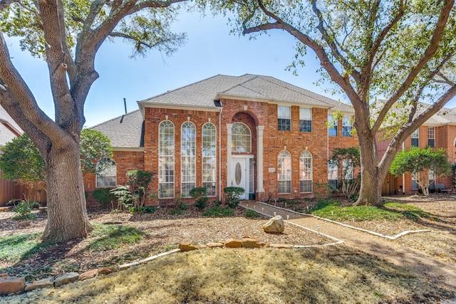 view of front of house featuring brick siding, a shingled roof, and fence