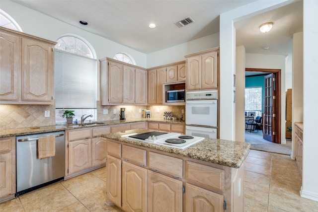 kitchen with light stone countertops, plenty of natural light, a sink, light brown cabinetry, and stainless steel appliances