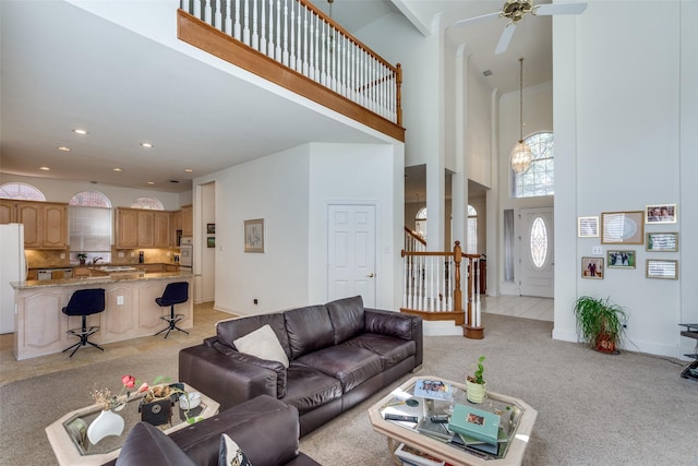 living room featuring light carpet, ceiling fan, stairs, and a towering ceiling