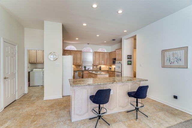 kitchen featuring washer / clothes dryer, white appliances, a breakfast bar area, decorative backsplash, and light stone countertops