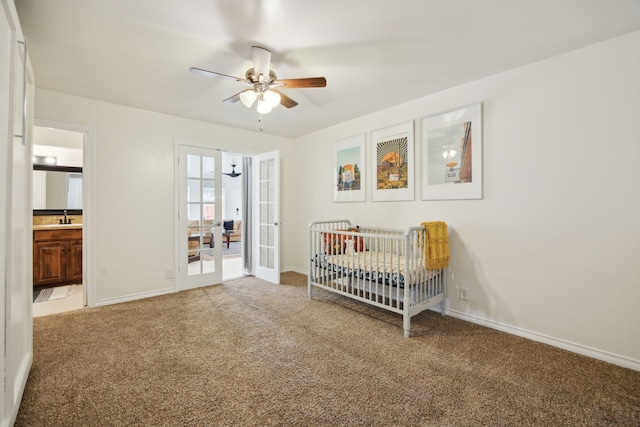 unfurnished bedroom with a crib, baseboards, light carpet, french doors, and a sink