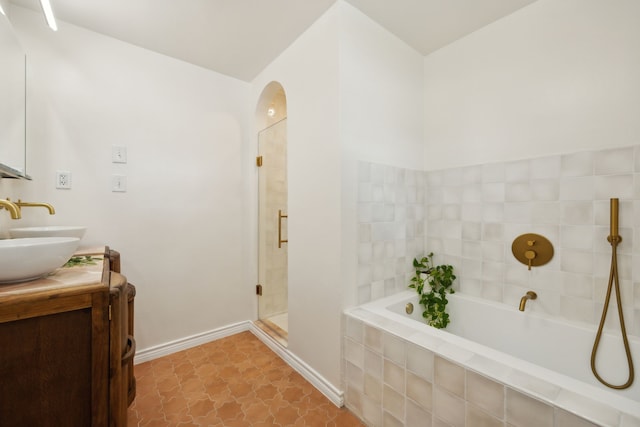 full bathroom with a shower stall, baseboards, a garden tub, double vanity, and a sink