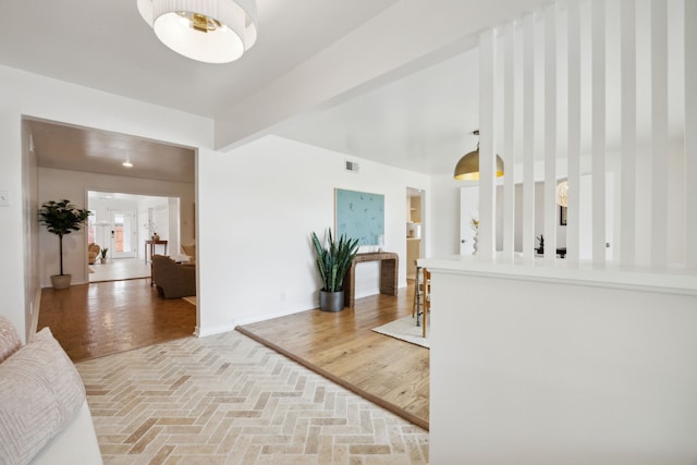 hallway featuring brick floor, baseboards, beam ceiling, and visible vents