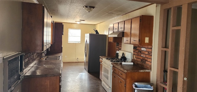 kitchen featuring under cabinet range hood, a sink, dark countertops, white gas range oven, and brown cabinetry