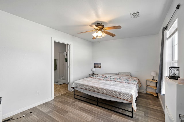 bedroom featuring connected bathroom, wood finished floors, visible vents, and baseboards