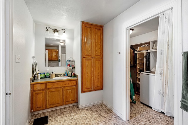 bathroom with vanity, baseboards, washer / clothes dryer, a textured ceiling, and a walk in closet