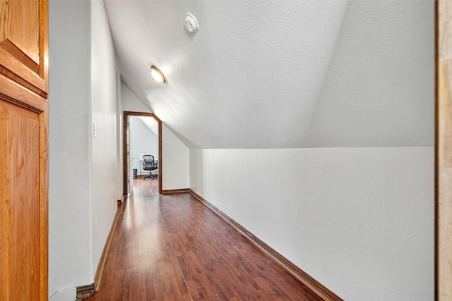 hall featuring dark wood finished floors, vaulted ceiling, baseboards, and a textured ceiling