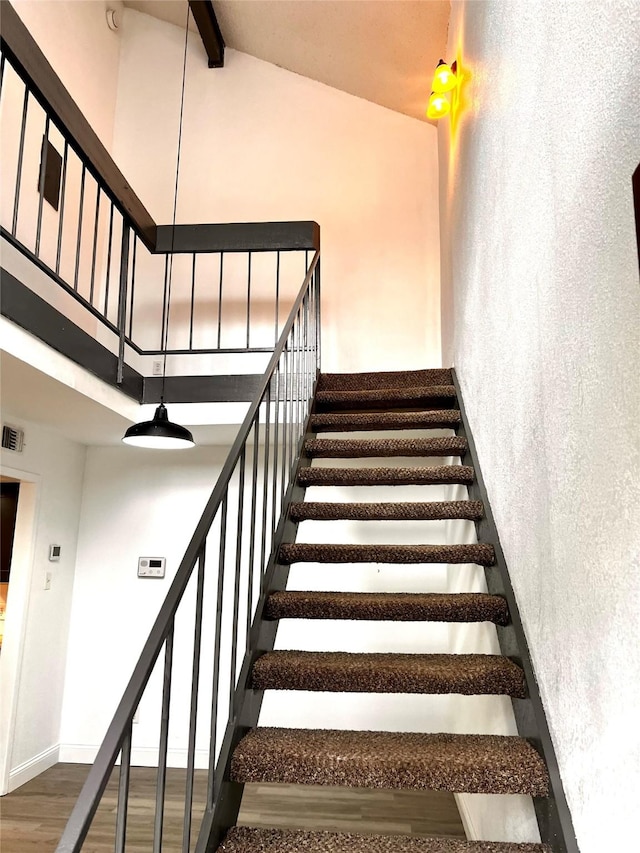 stairs featuring wood finished floors, visible vents, baseboards, a high ceiling, and beamed ceiling