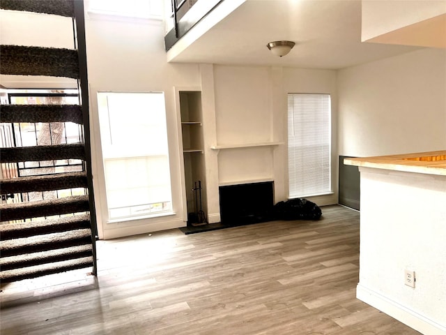 unfurnished living room featuring stairs, a fireplace with raised hearth, baseboards, and light wood finished floors