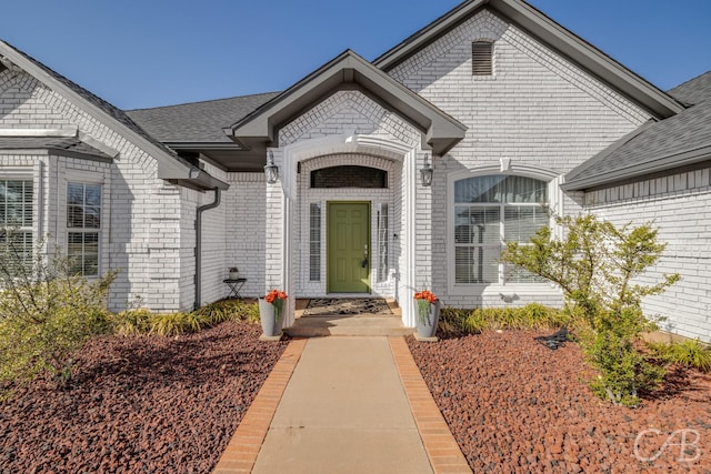 property entrance featuring brick siding and a shingled roof