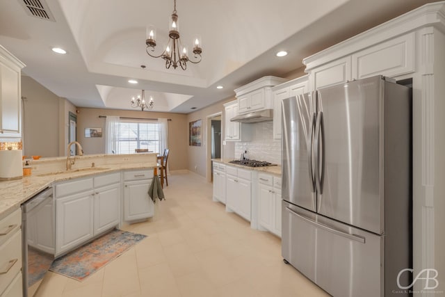 kitchen with a sink, a tray ceiling, stainless steel appliances, an inviting chandelier, and white cabinets