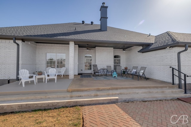 rear view of house with brick siding, a patio area, a ceiling fan, and roof with shingles