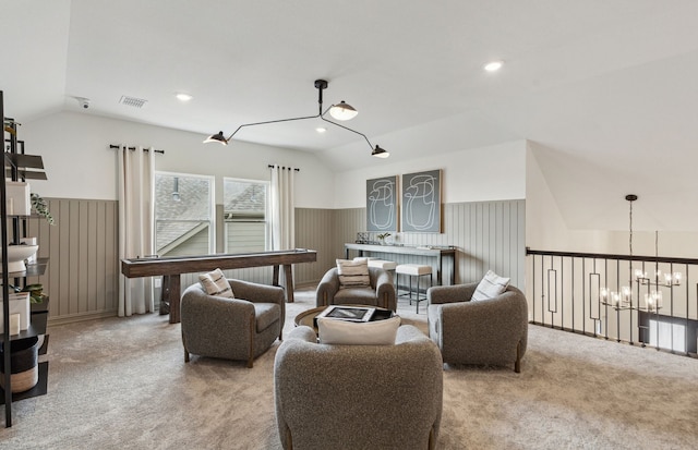 carpeted living room featuring an inviting chandelier, lofted ceiling, visible vents, and a wainscoted wall