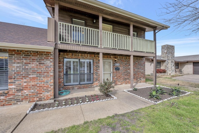 exterior space with a balcony, brick siding, and roof with shingles