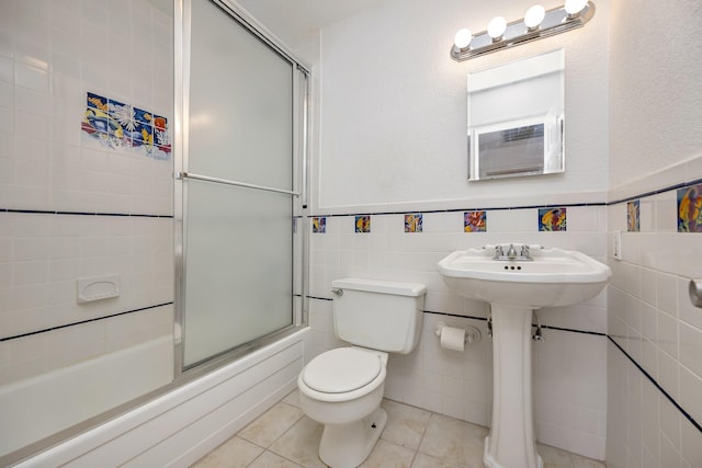 bathroom with tile patterned floors, toilet, shower / bath combination with glass door, tile walls, and wainscoting